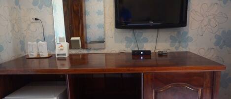 Un escritorio de madera con un televisor de pantalla plana, un refrigerador pequeño y un altavoz.