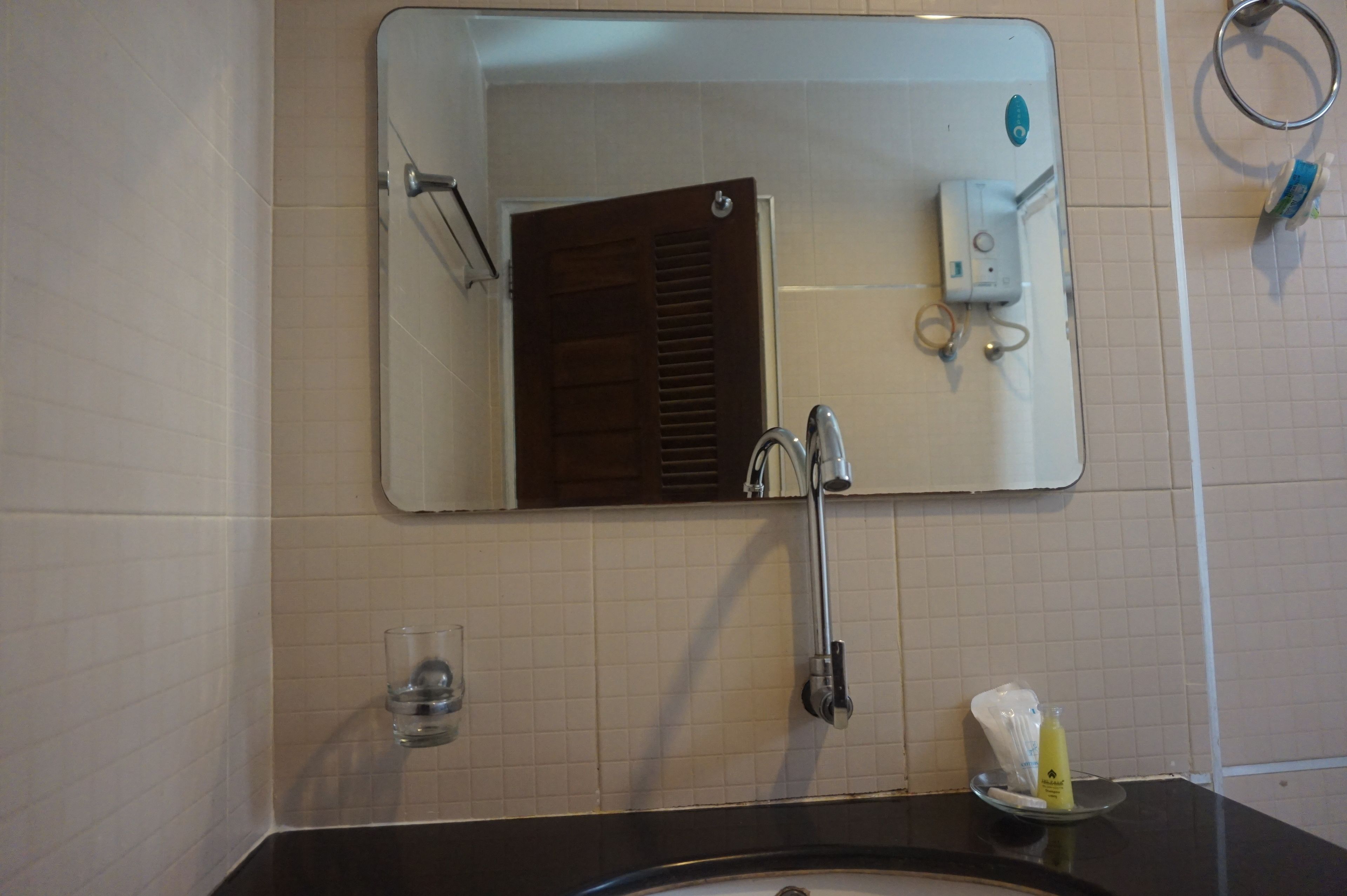A bathroom with a mirror, a sink, a towel rack, and a glass of water.