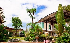 A modern building with a covered outdoor area, surrounded by lush tropical plants and a small water feature. - The Park Nangrong Resort (Nang Rong)
