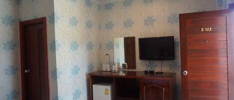 A bedroom with a wooden wardrobe, a television mounted on the wall, and a small refrigerator.