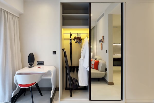 Et moderne hotelværelse med skrivebord, stol og et walk-in closet med hængende tøj og badekåbe.