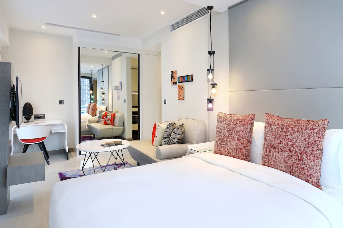 A modern hotel room with a large bed, a seating area with a sofa and armchairs, a small table, and a TV.
