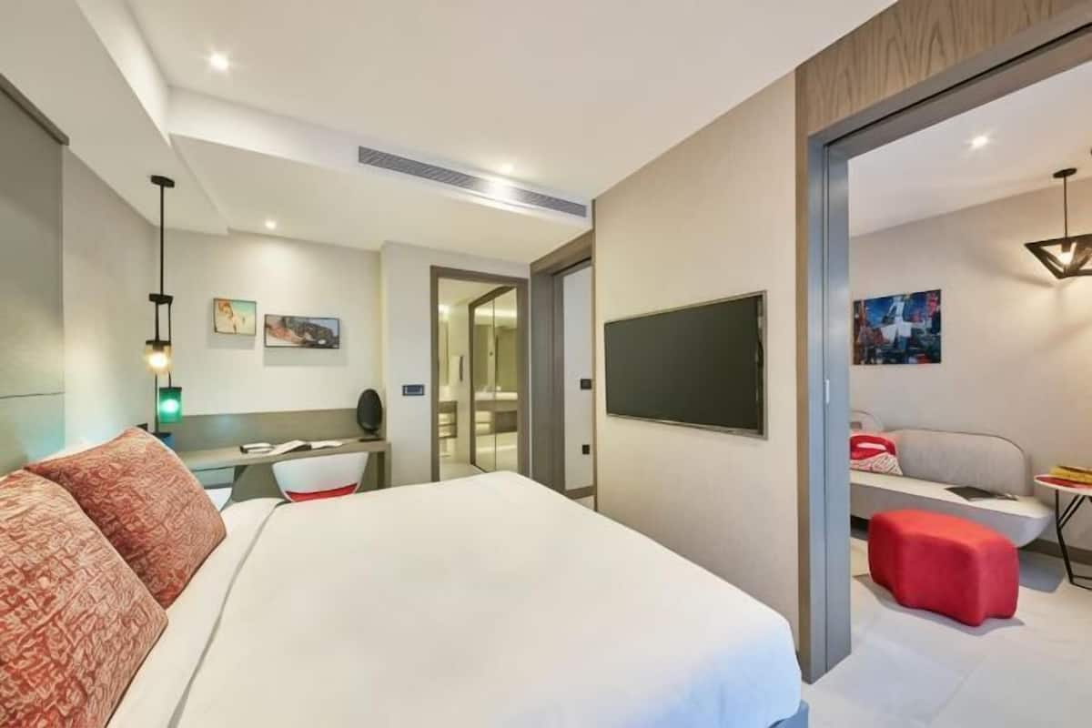 A modern hotel room with a large bed, a desk, a TV, and a sofa.