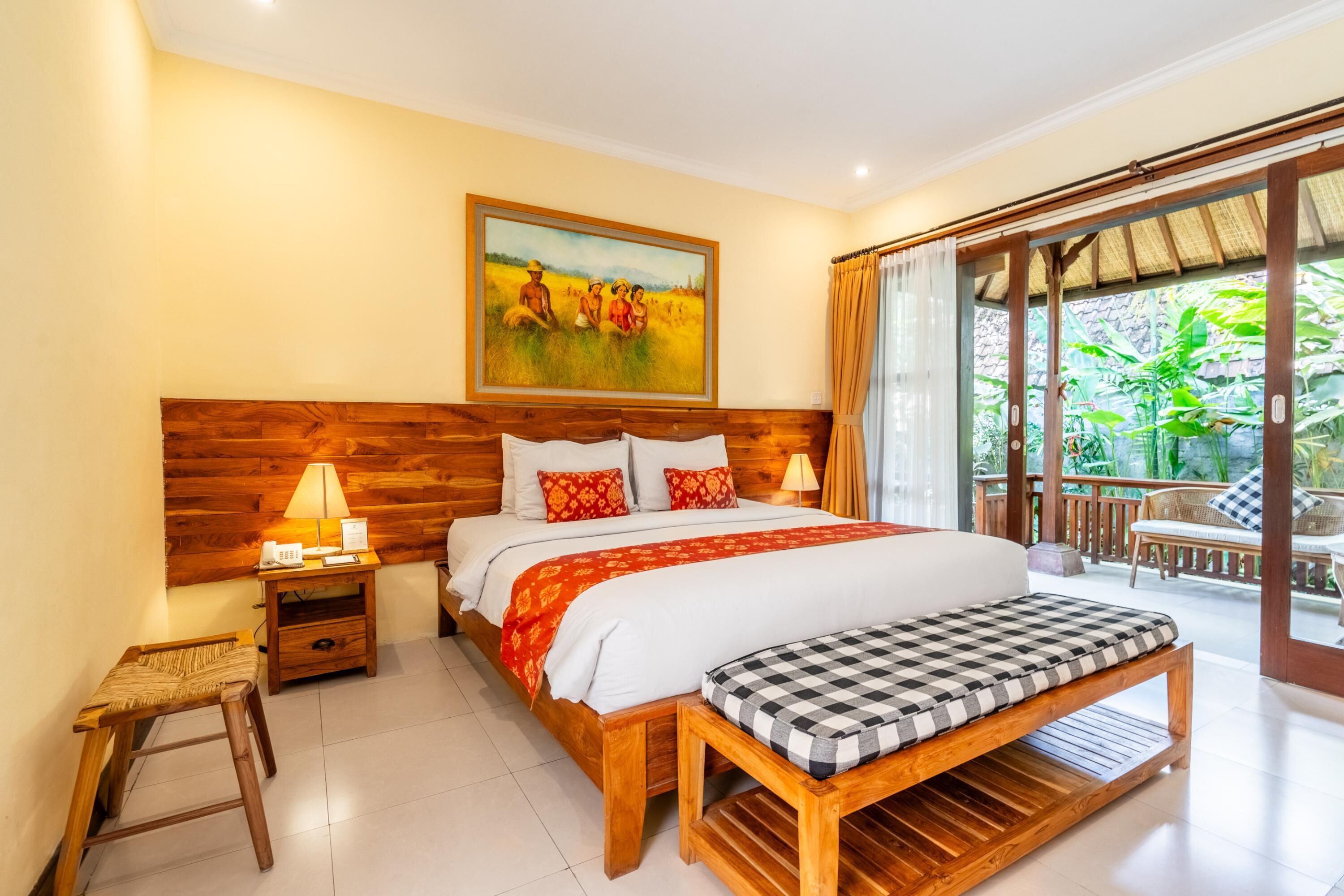 Un dormitorio con cabecera de madera, una cama grande con colcha roja y blanca, un banco al pie de la cama y un cuadro sobre la cama.