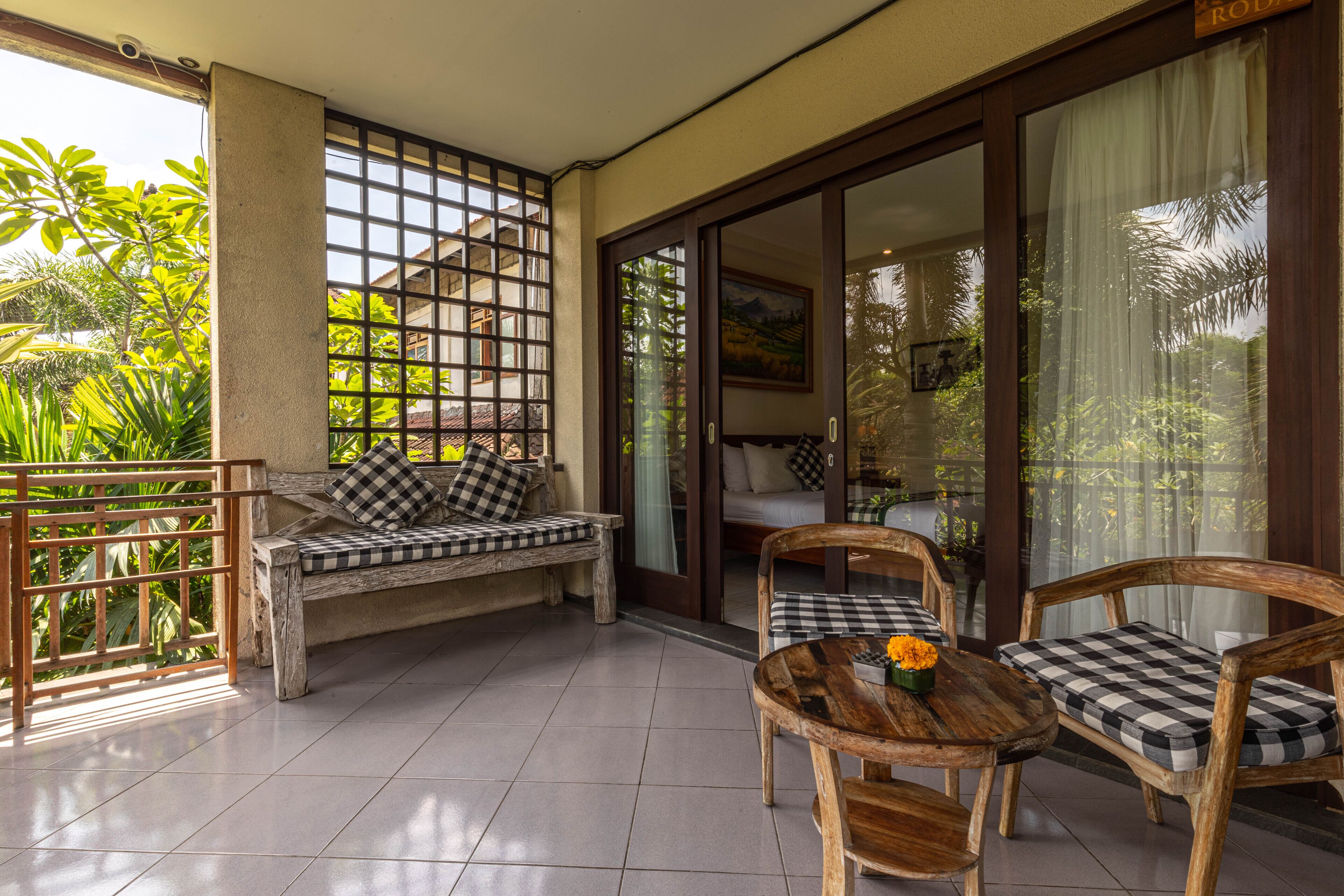 Ein Balkon mit einer karierten Couch, Holzstühlen und einem kleinen Tisch mit Blumen.