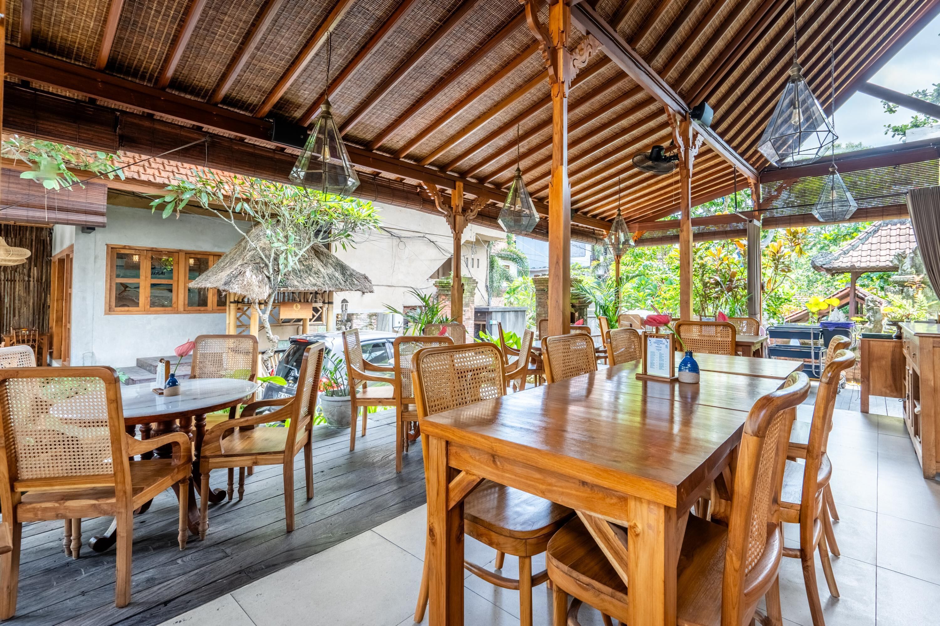 Un espace de restauration en plein air avec des tables et des chaises en bois, un toit de chaume et des luminaires suspendus.