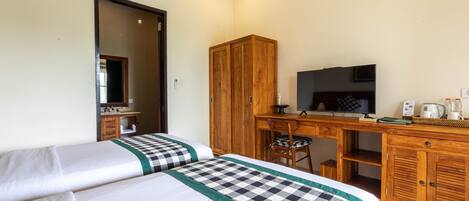 A hotel room with two beds, a wooden desk with a television, a chair, and a wardrobe.