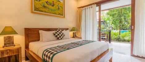 A spacious bedroom with a large bed, wooden headboard, and a painting above it. There are two bedside tables with lamps, and a view of a garden through a sliding door.