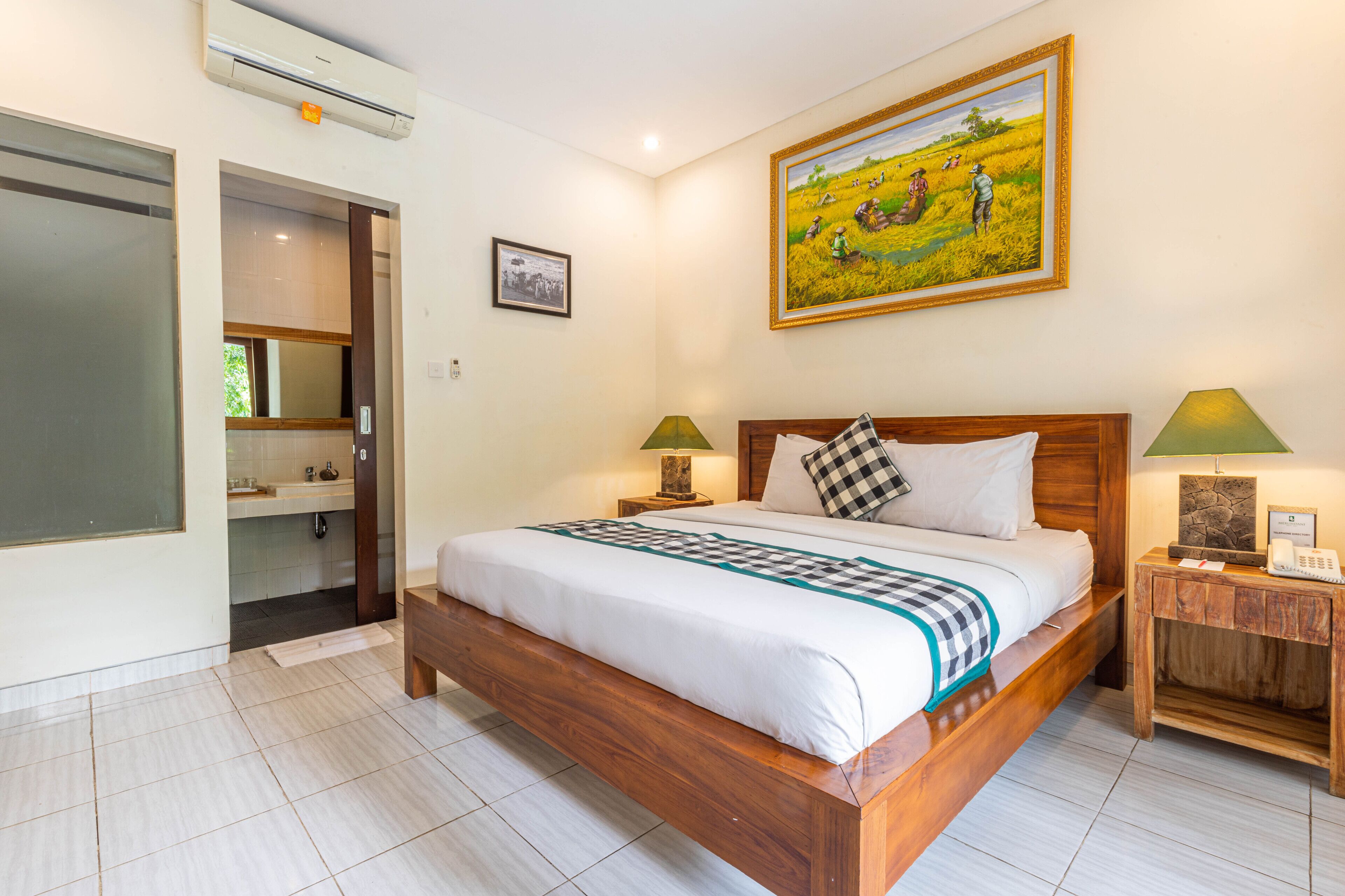 Habitación de hotel con cama de madera, dos mesitas de noche con lámparas, un cuadro en la pared y un baño visible a través de una puerta abierta.