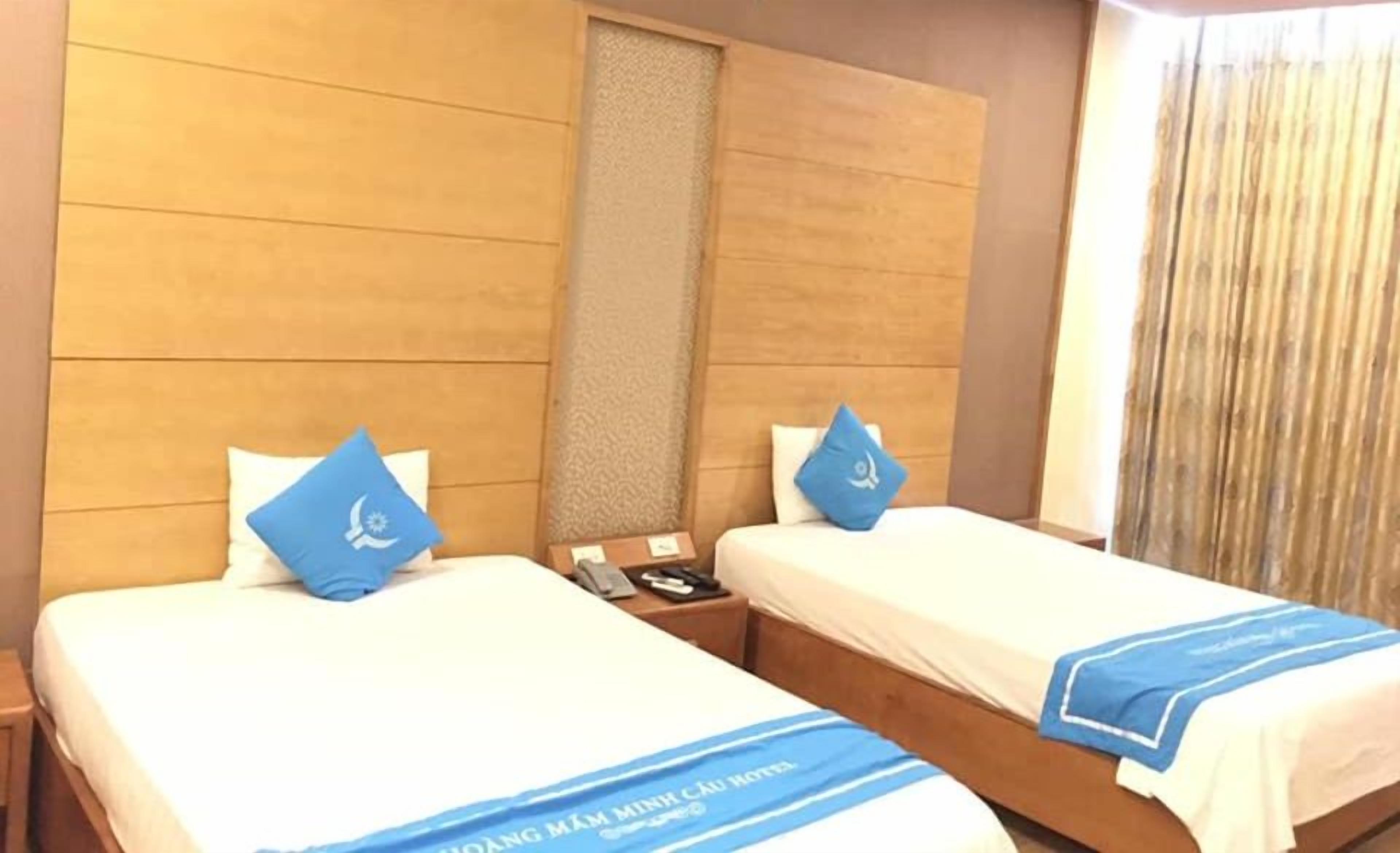 A standard twin bed room with two beds, each with a blue pillow and a blue bedspread.