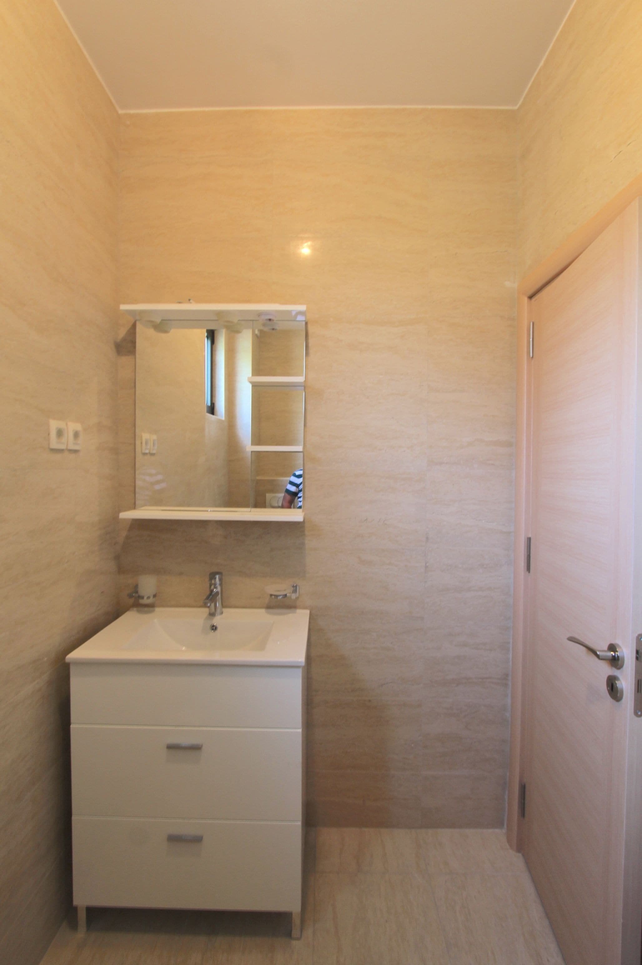 Un baño pequeño y moderno con tocador blanco, un espejo y una puerta.