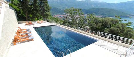 Piscina con sillas de descanso y vistas a montañas y una ciudad.