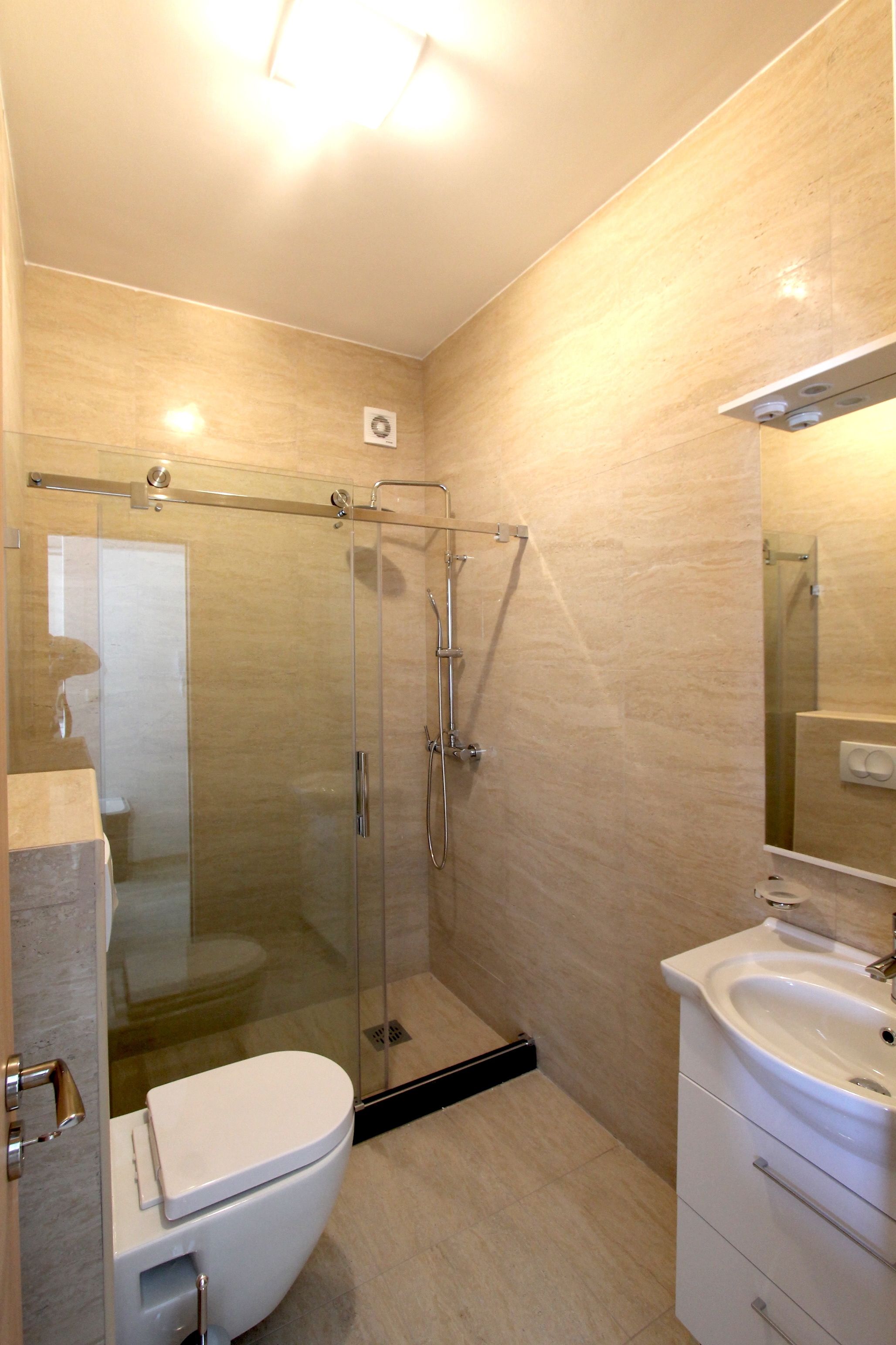 A modern bathroom with a glass-enclosed shower, a white toilet, and a sink with a mirror above it.