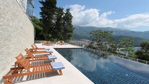 Une piscine à débordement située sur le toit, avec des chaises longues en bois et une vue sur les montagnes.