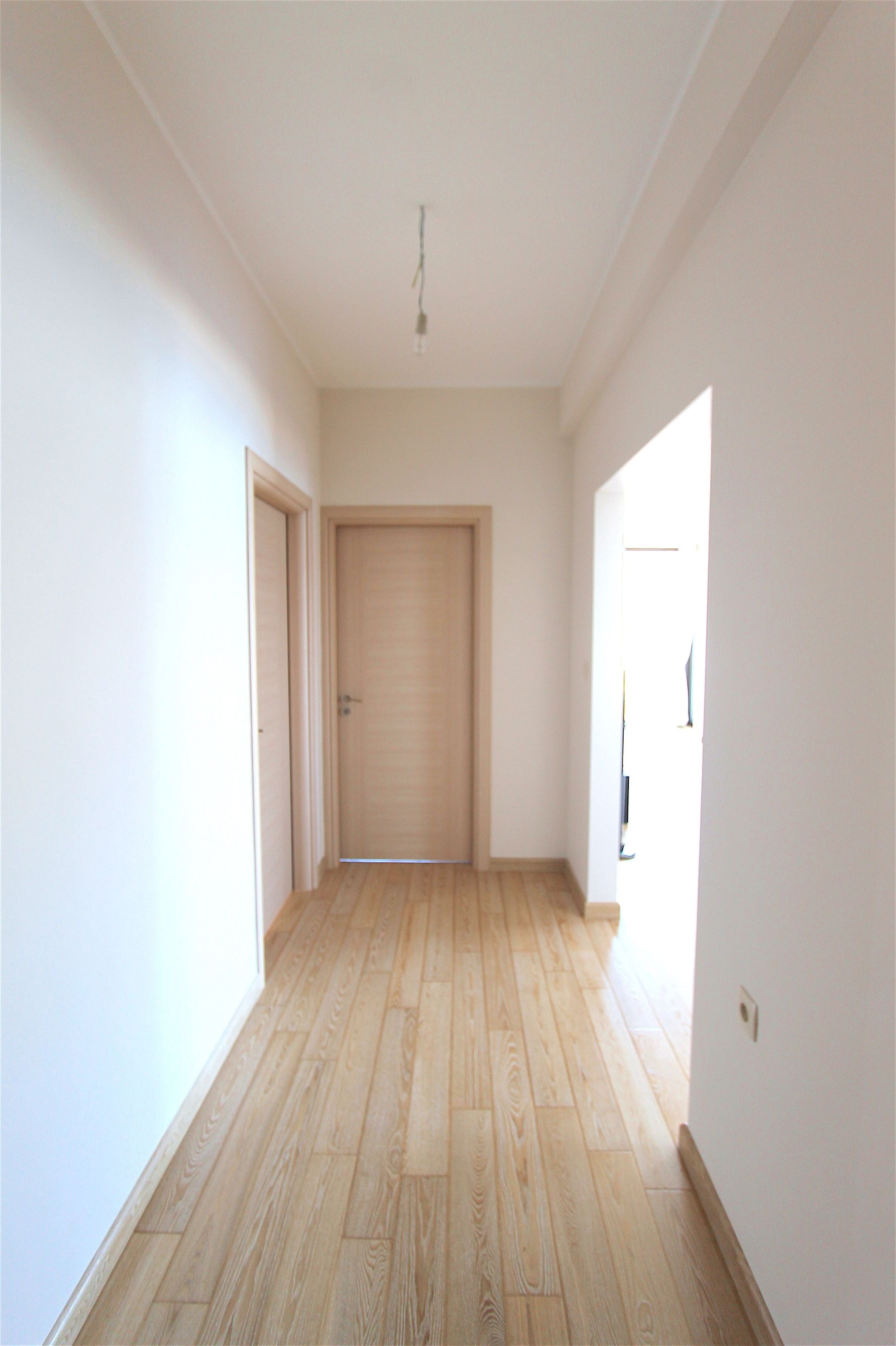 A hallway with wooden flooring, white walls, and a closed door at the end.