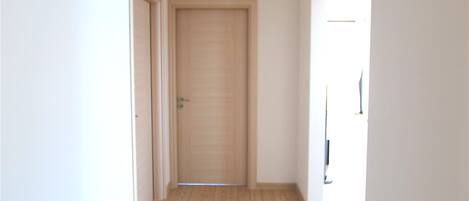 A hallway with wooden flooring, white walls, and a closed door at the end.