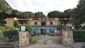 A two-story building with a yellow facade, a gated entrance, outdoor seating area, and a staircase leading to the upper floor. - Hotel Paradiso (Tarquinia)