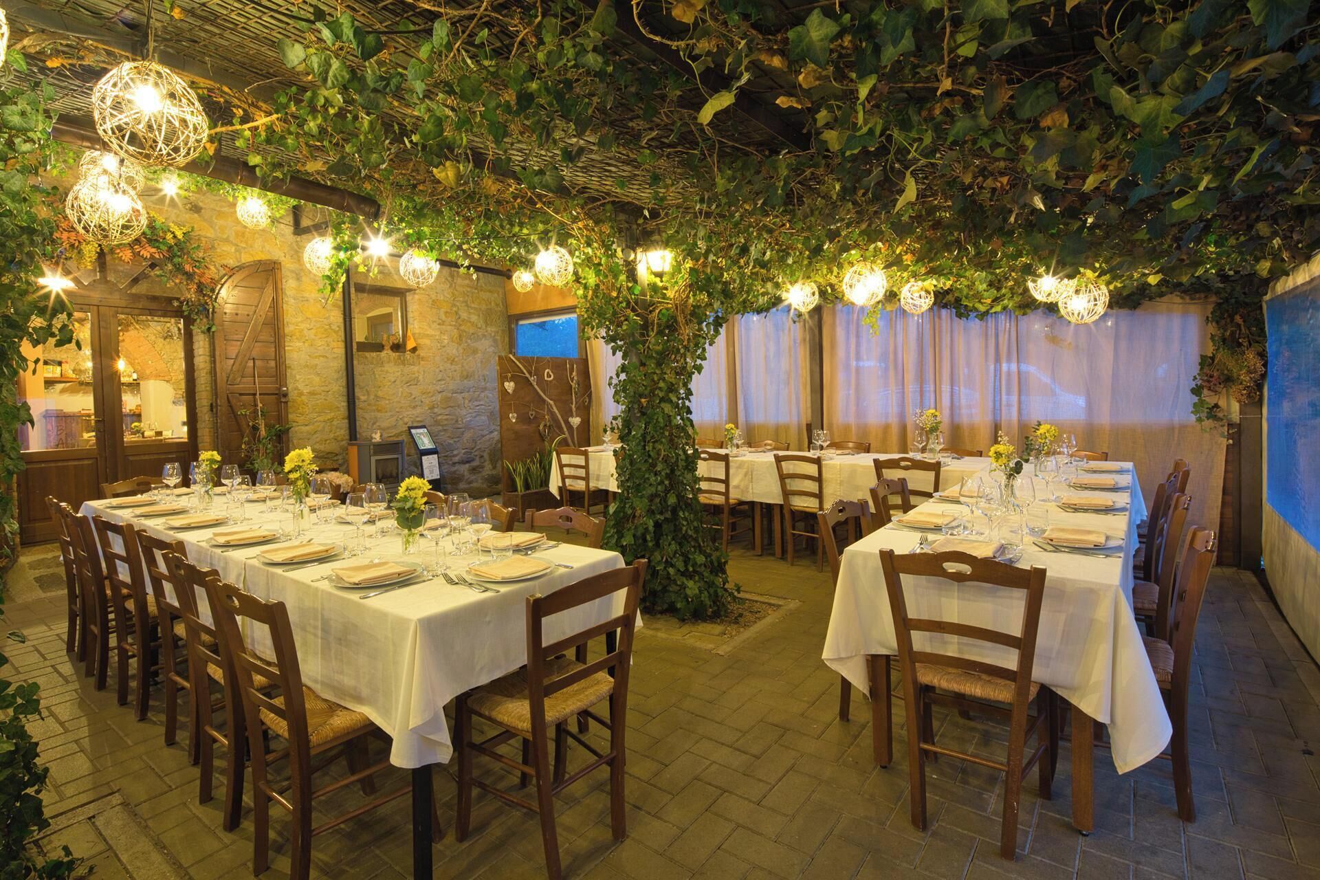 Un'area pranzo interna con tavoli apparecchiati, circondata da piante e pareti in pietra.