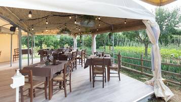 An outdoor dining area with wooden tables and chairs under a covered structure with hanging lights.