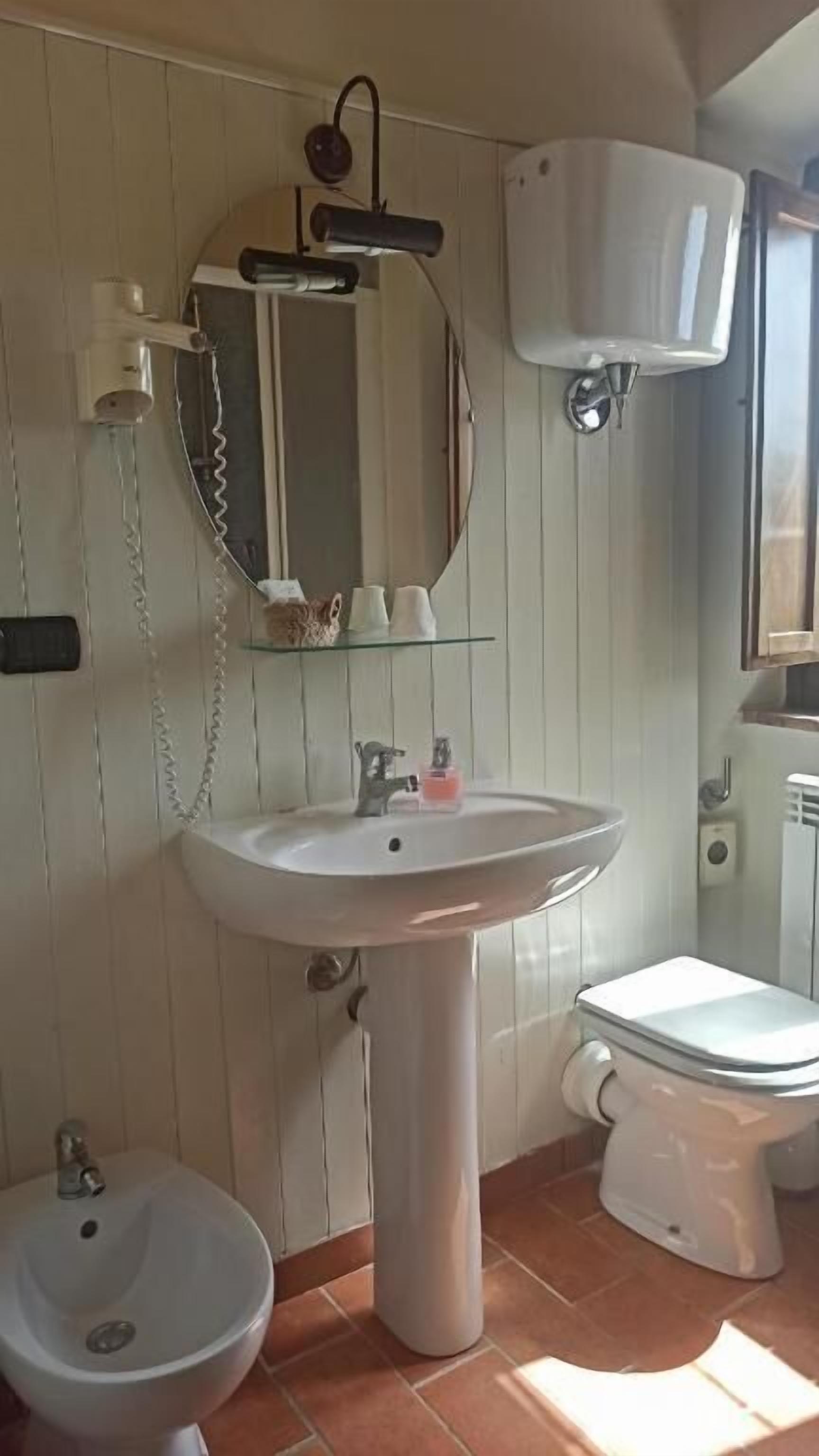 Un baño con lavamanos pedestal, inodoro, bidé y espejo.