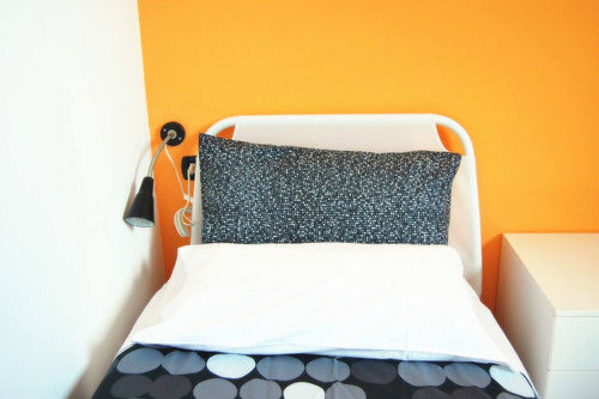 A bed with a white headboard and a grey pillow in a room with orange walls.