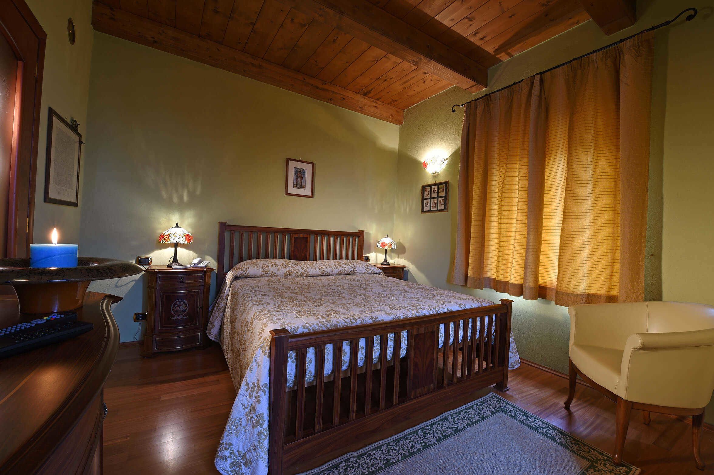 A bedroom with a wooden bed, two bedside lamps, a chair, and a desk with a candle.