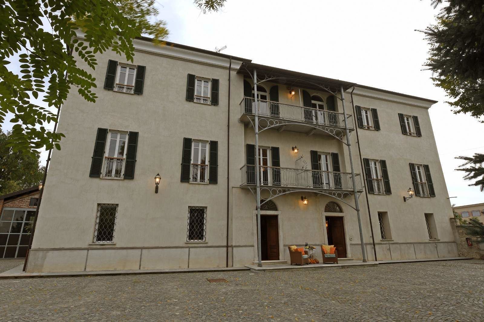 Un edificio a due piani con un balcone, diverse finestre con persiane e un basamento in pietra.