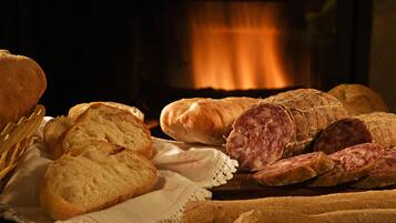 Diverse varietà di pane e salumi su un tavolo, con un camino sullo sfondo.