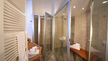 A modern bathroom with a glass-enclosed shower, a wooden bench, and a wicker chair.