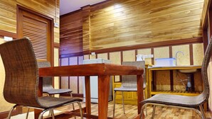 Habitació amb panells de fusta, una taula de fusta i dues cadires. Es veu un rentaplat amb un vàter i una bacineta blanca al fons.