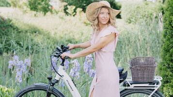 A person standing next to a bicycle with a basket, in a grassy area with flowers and trees.