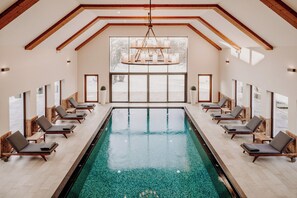 A large indoor swimming pool with a wooden ceiling and a chandelier, surrounded by lounge chairs. - Der Eisvogel - Wellness- & Genusshotel  (Neustadt an der Donau)