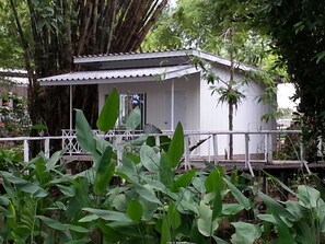 A small white building with a porch, surrounded by lush greenery and a large tree. - Hadsaisuay Resort (Kanchanaburi)