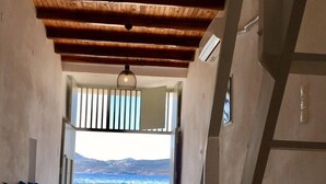 Una stanza con soffitto in legno, vista sul mare, un divano con cuscini, una poltrona e un tavolino.