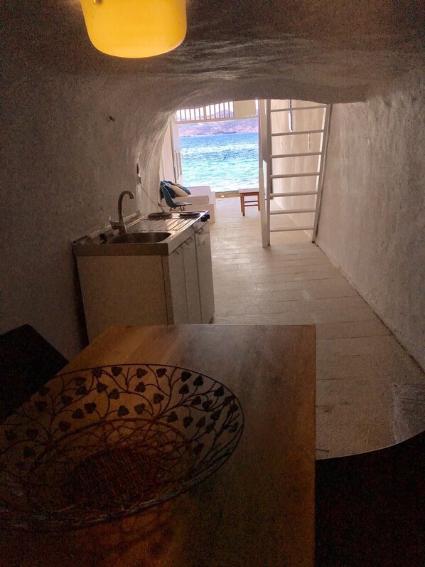 A narrow, enclosed space with a sink, a chair, and a view of the sea through a door. - Klima House (Milos)