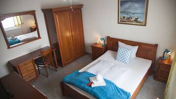 A hotel room with a bed, a desk, a chair, a wardrobe, a nightstand, and a painting on the wall.