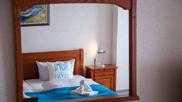 A neatly made bed with a blue blanket and a pillow with text, a wooden nightstand with a lamp, and a painting on the wall.