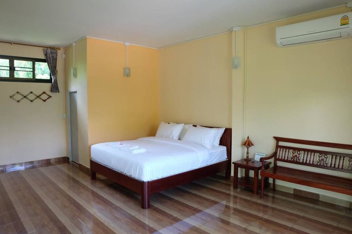 Un dormitorio con cama de madera, una mesita de noche, un banco y un equipo de aire acondicionado.
