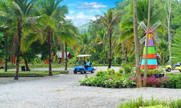 Un resort tropical con palmeras, un molino de viento de colores y un carrito de golf sobre un camino de grava.