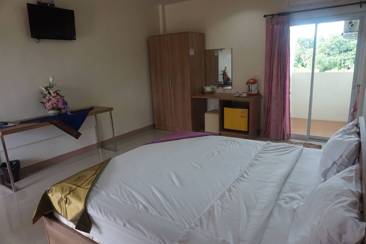 Un dormitorio con cama, escritorio, armario, espejo y puerta corredera a un balcón.