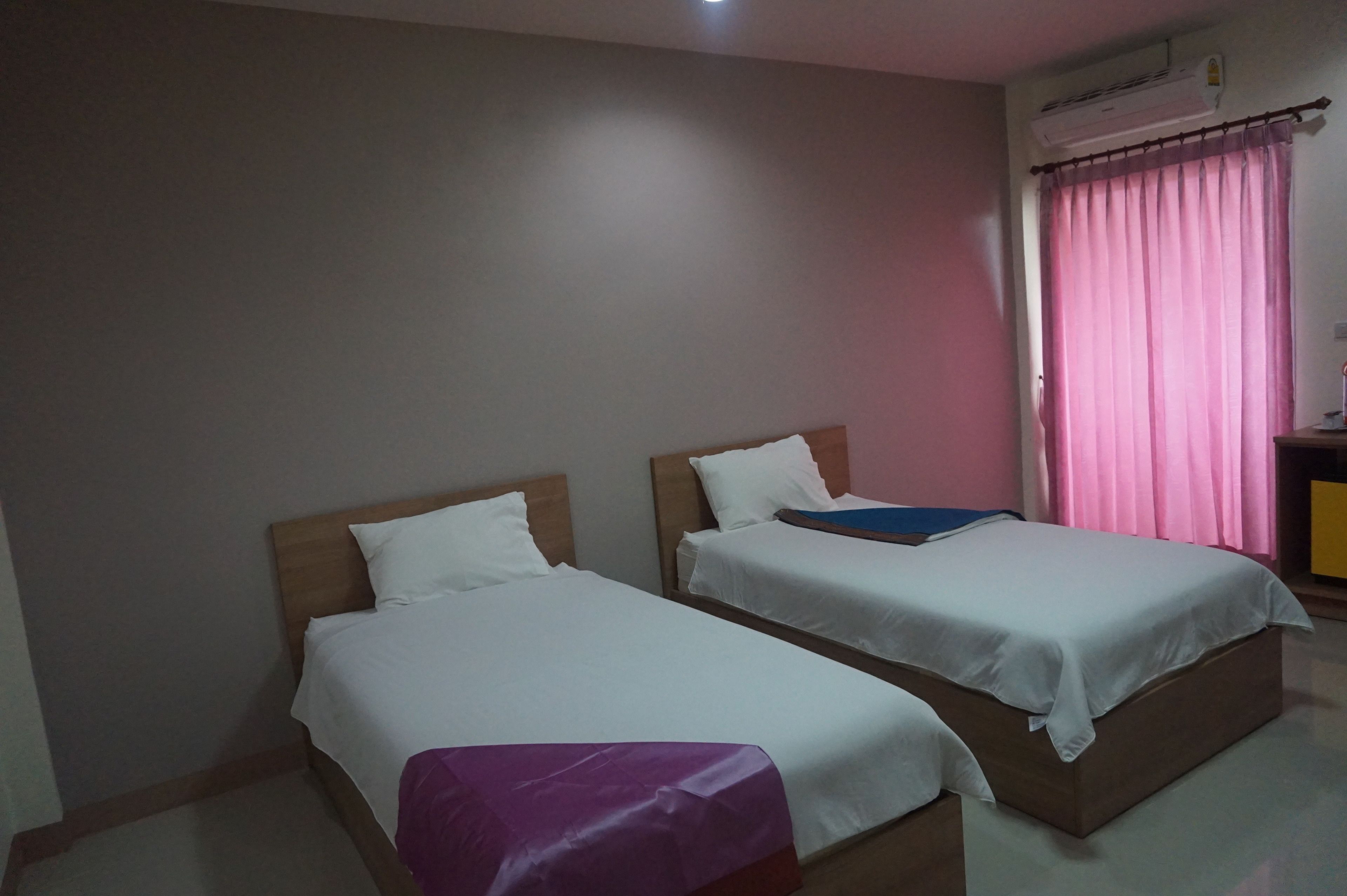 A room with two single beds, a wooden headboard, a pink curtain, and a small table with a lamp.