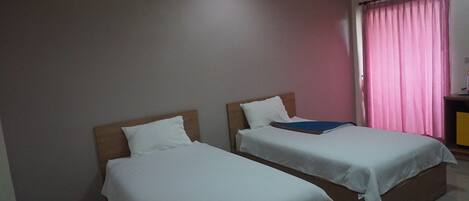 A room with two single beds, a wooden headboard, a pink curtain, and a small table with a lamp.