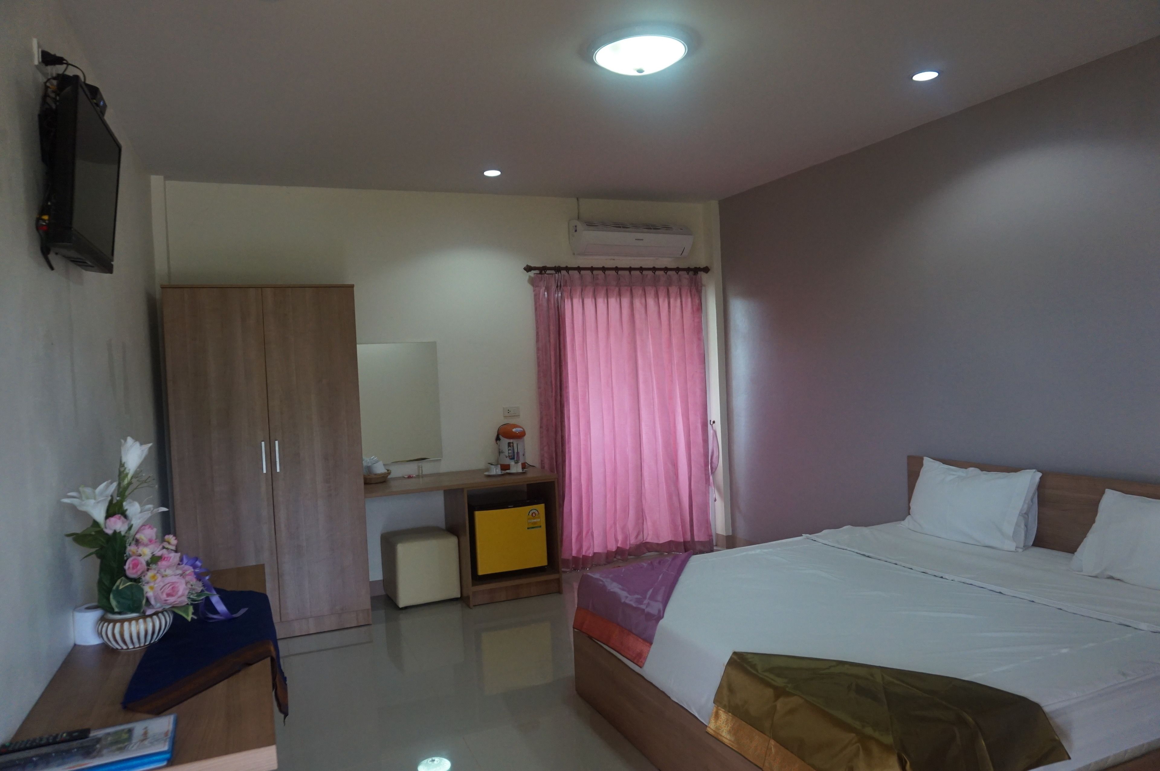 A hotel room with a bed, a desk, a wardrobe, and an air conditioning unit.