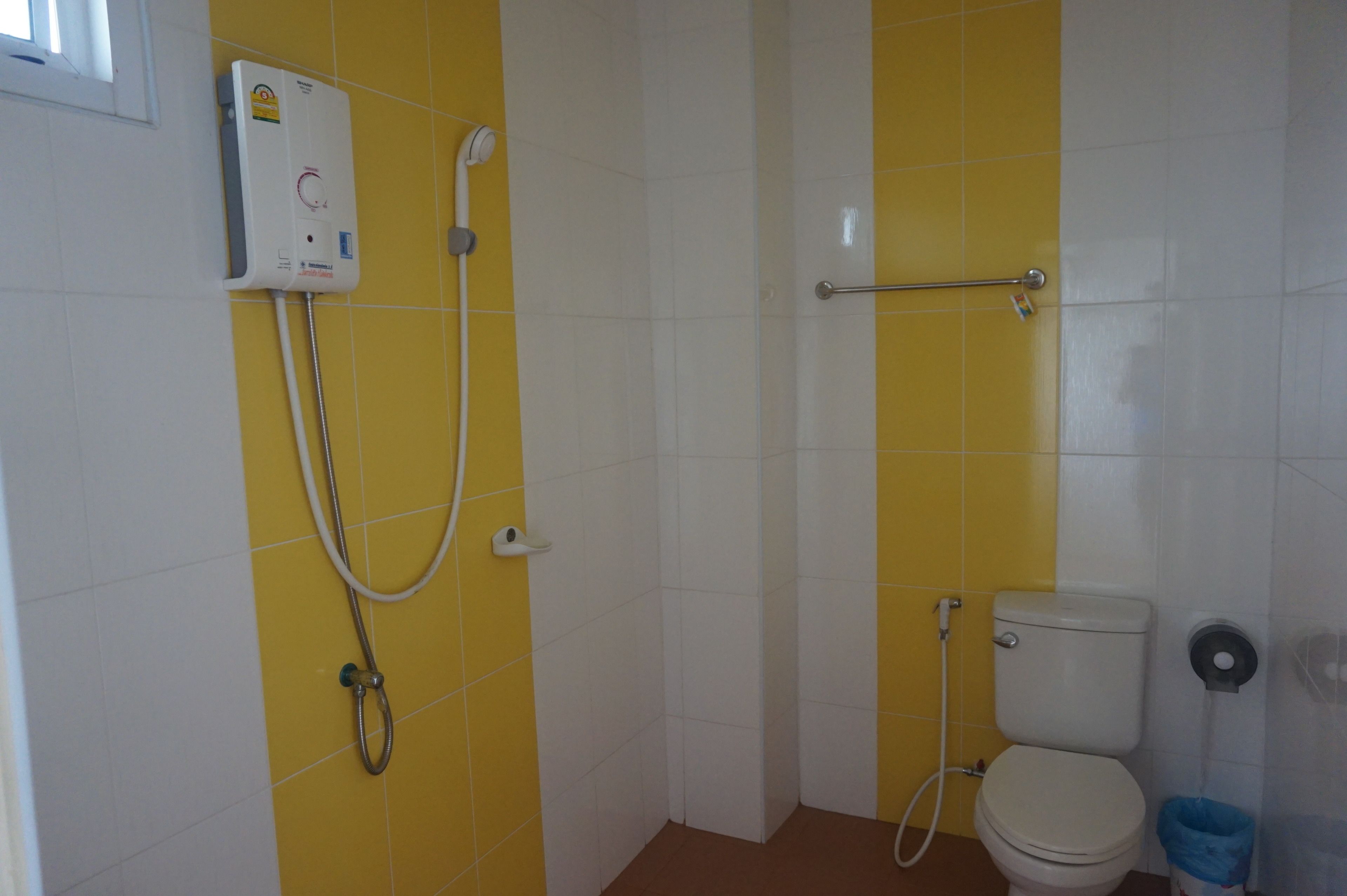 A bathroom with yellow and white tiles, a white toilet, a shower unit, and a blue trash bin.