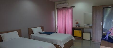 A hotel room with two beds, a desk, a mirror, an air conditioner, and a pink curtain.