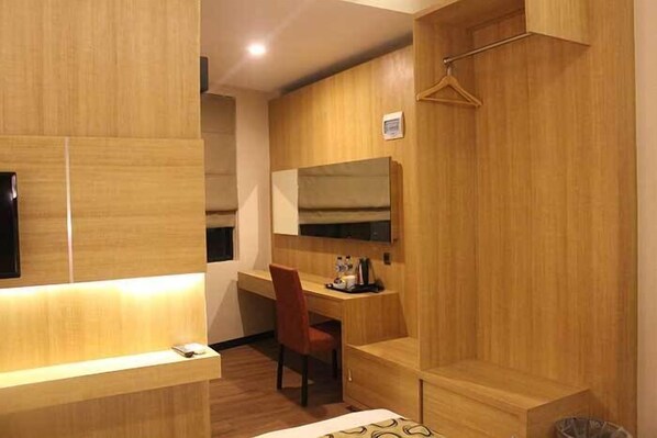 Une chambre d’hôtel avec un bureau en bois, une chaise, un lit, une télévision et un miroir.