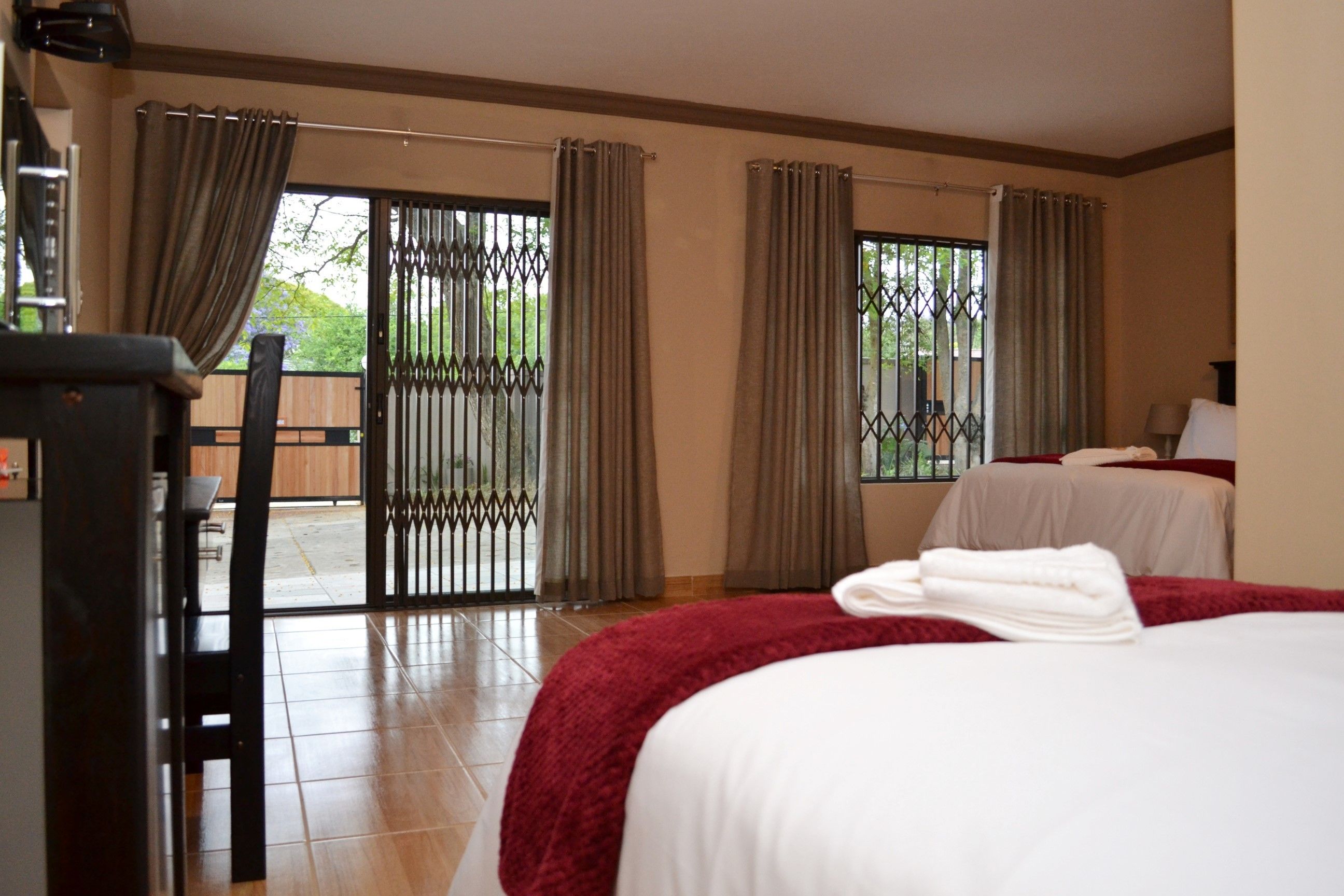A hotel room with a bed, a desk, and a view through a window with curtains.