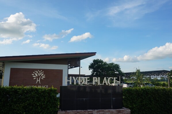 A sign for Hyde Place with a tree logo, surrounded by greenery and a clear sky. - Hyde Place Resort (Buriram)