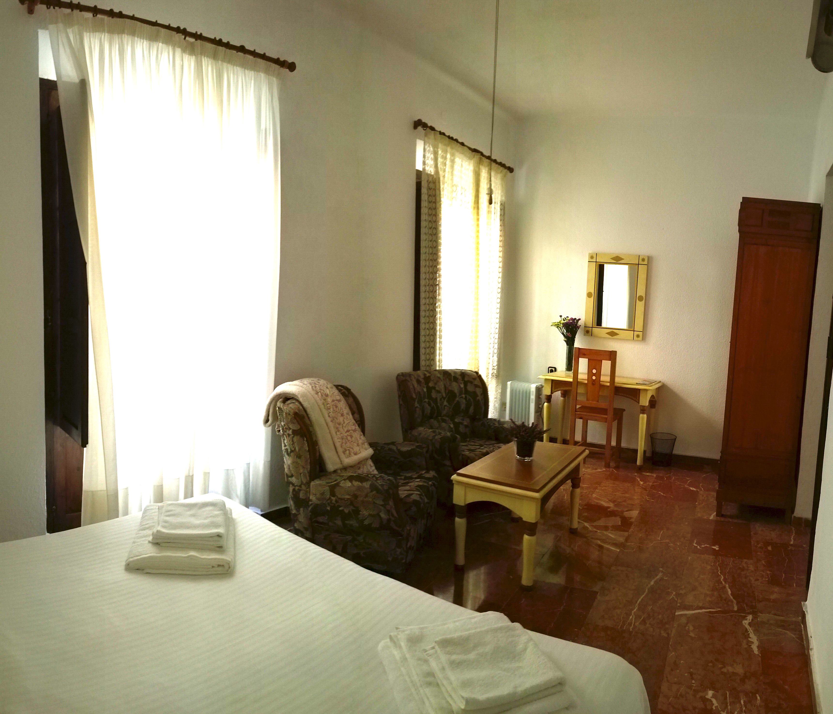A hotel room with a bed, a chair, a small table, a mirror, and a door.