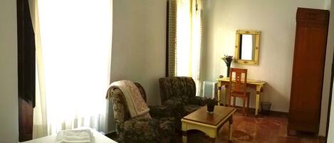 A hotel room with a bed, a chair, a small table, a mirror, and a door.